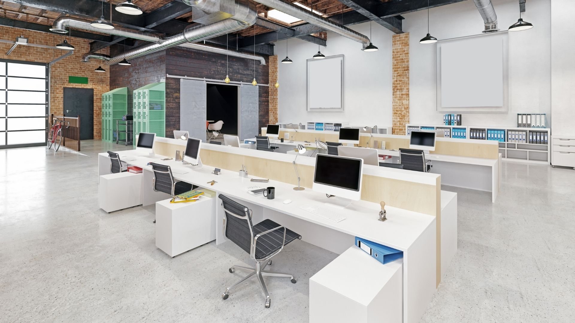 Modern industrial office space with computer workstations, exposed brick, and steel ductwork ceiling.