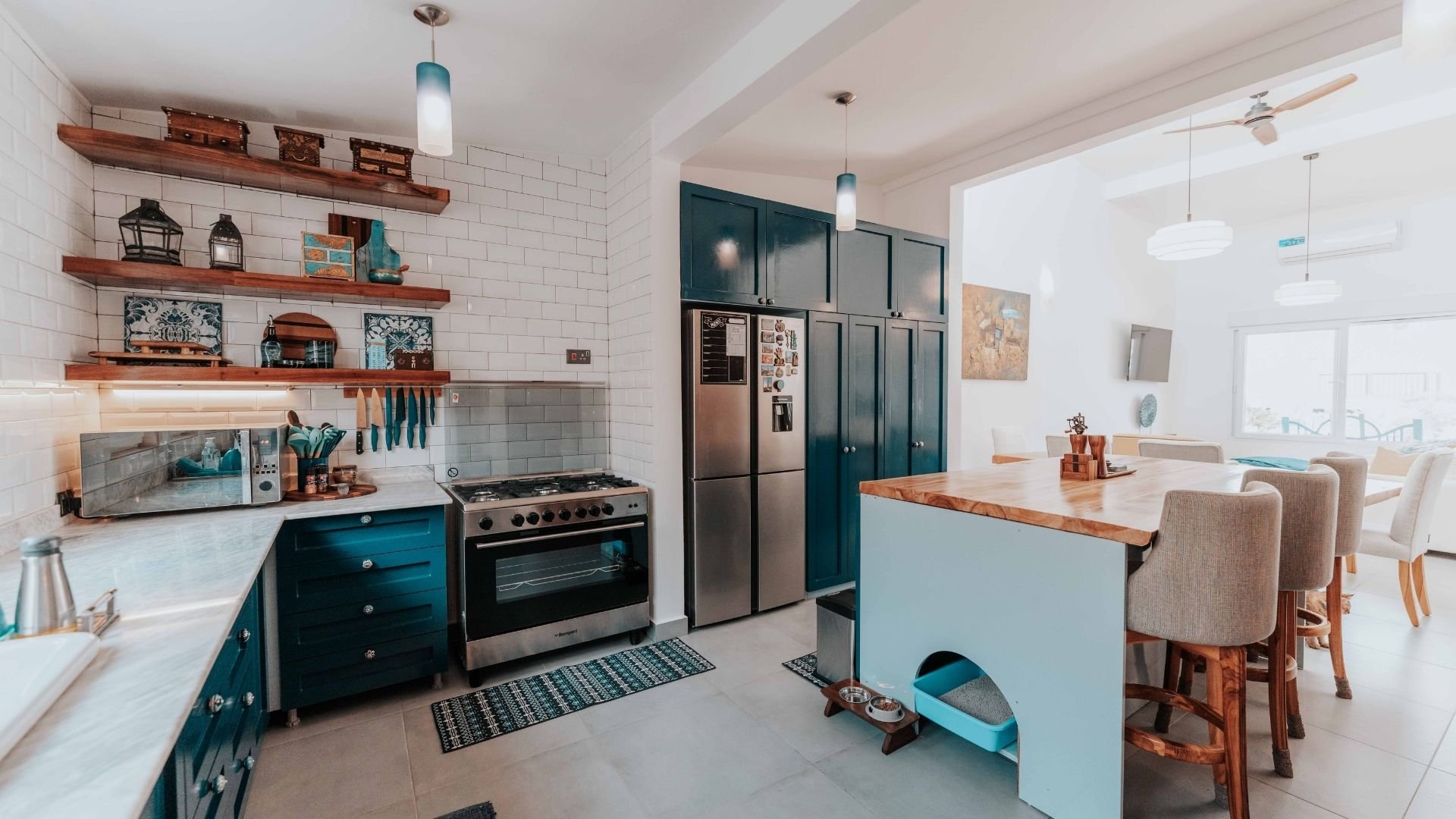 Modern kitchen with teal cabinets, white subway tiles, wooden shelves, and island with seating area