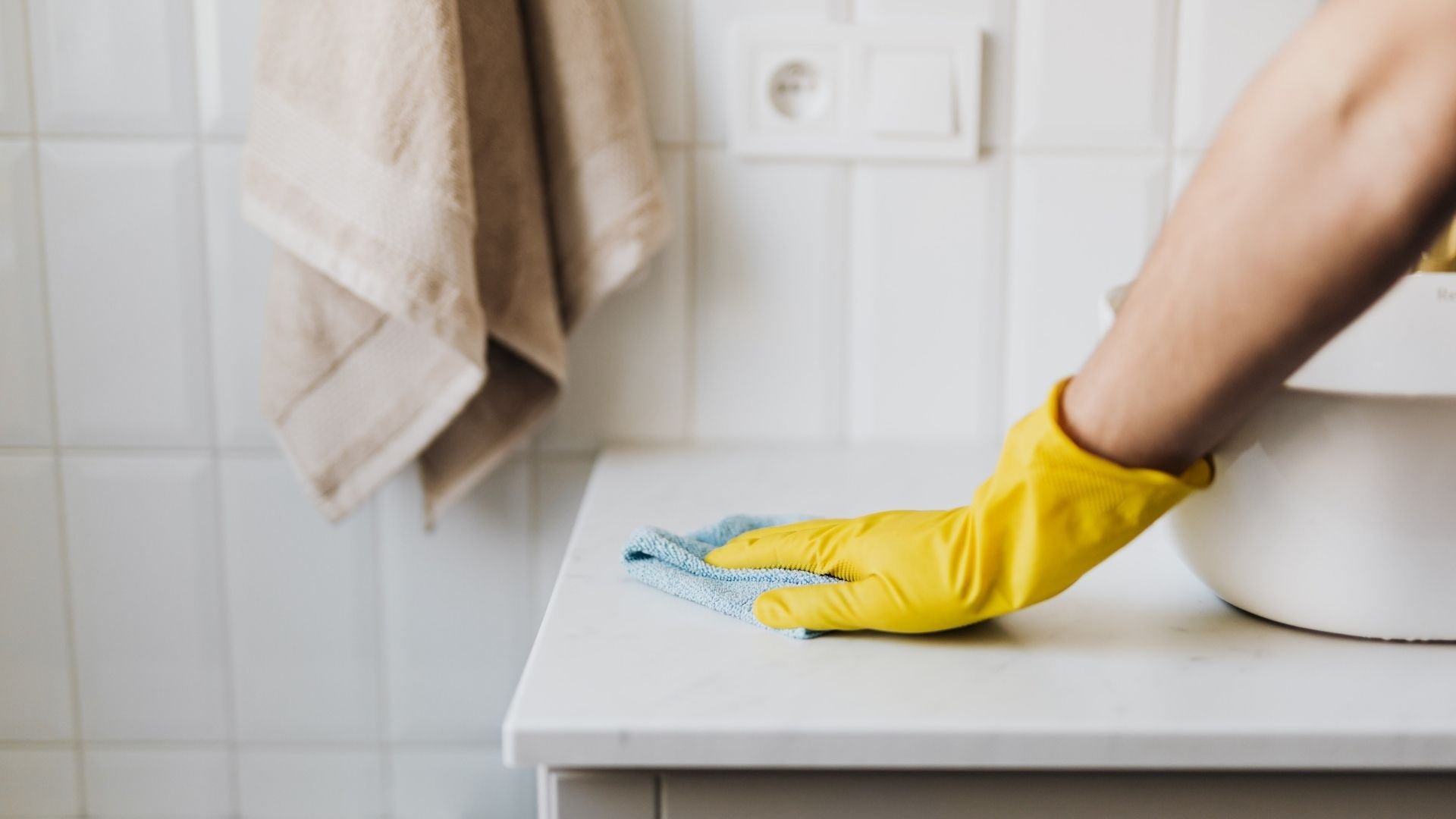 Person wearing yellow gloves cleaning bathroom countertop with blue cloth
