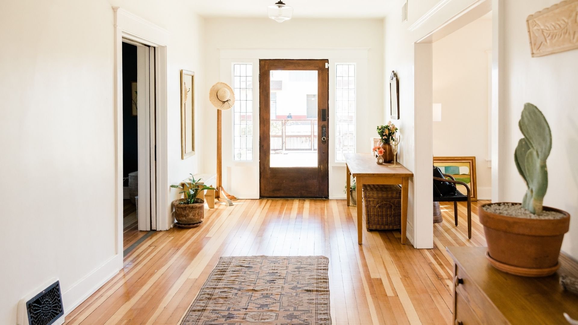 Bright entryway with wooden flooring, potted plants, and door leading to balcony view.