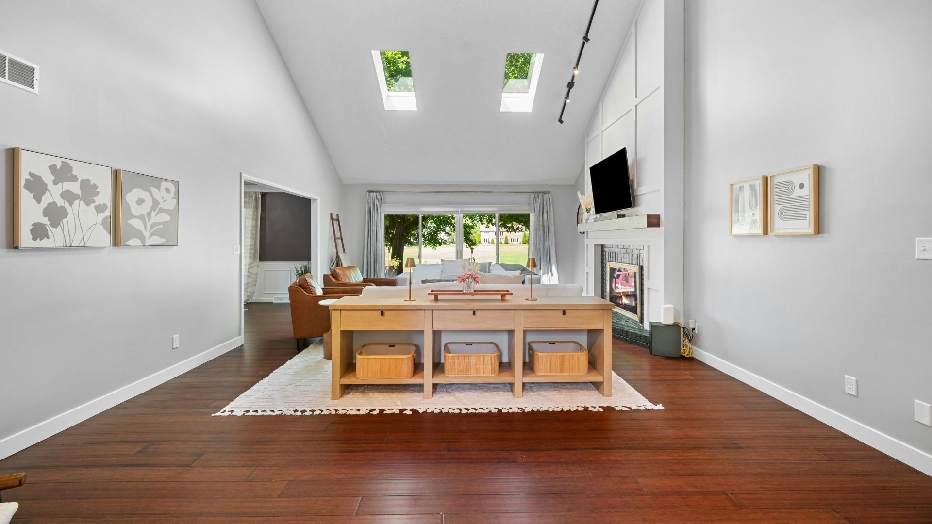 Bright modern living room with wooden console table, leather chair, and skylight windows overlooking garden