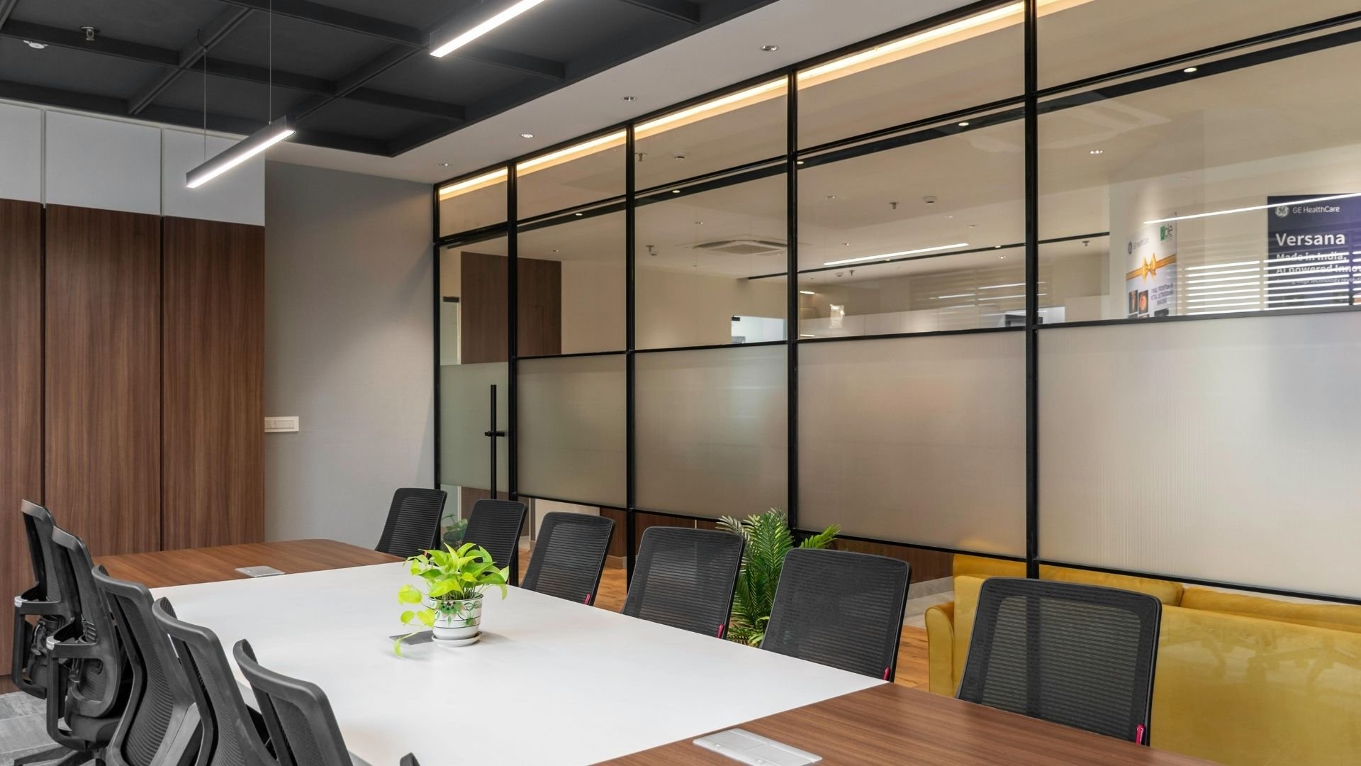 Modern office conference room with white table, black chairs, glass partitions, and wooden accents