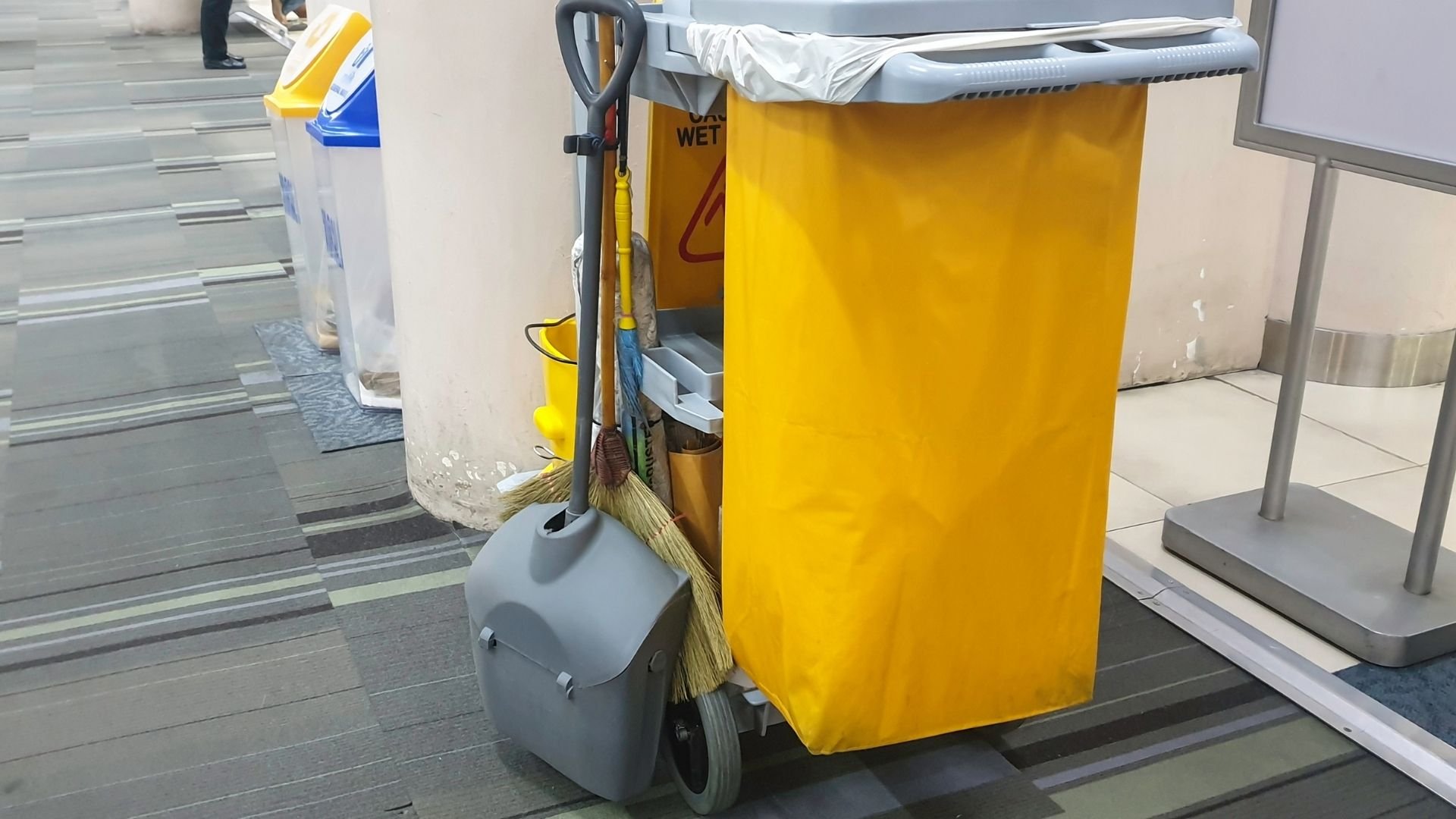 Cleaning supplies cart with yellow bag and mop handles in indoor facility