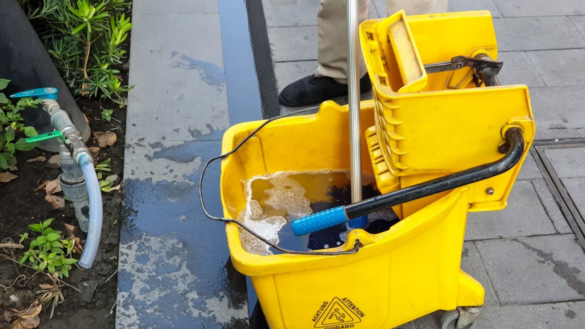 Yellow mop bucket with cleaning supplies and tools on wet floor